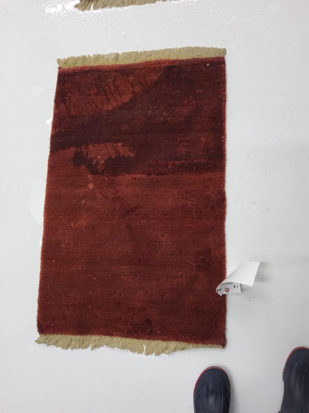 Red area rug with dark staining across the top, before cleaning